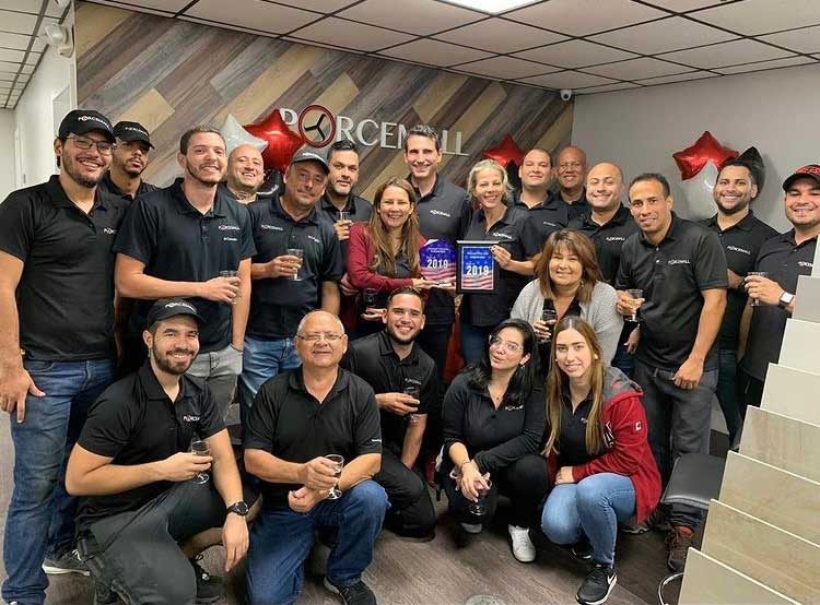 El equipo de Porcemall reunido en la oficina de Deerfield Beach bajo el mural del logo, con las placas del premio Best of Deerfield Beach