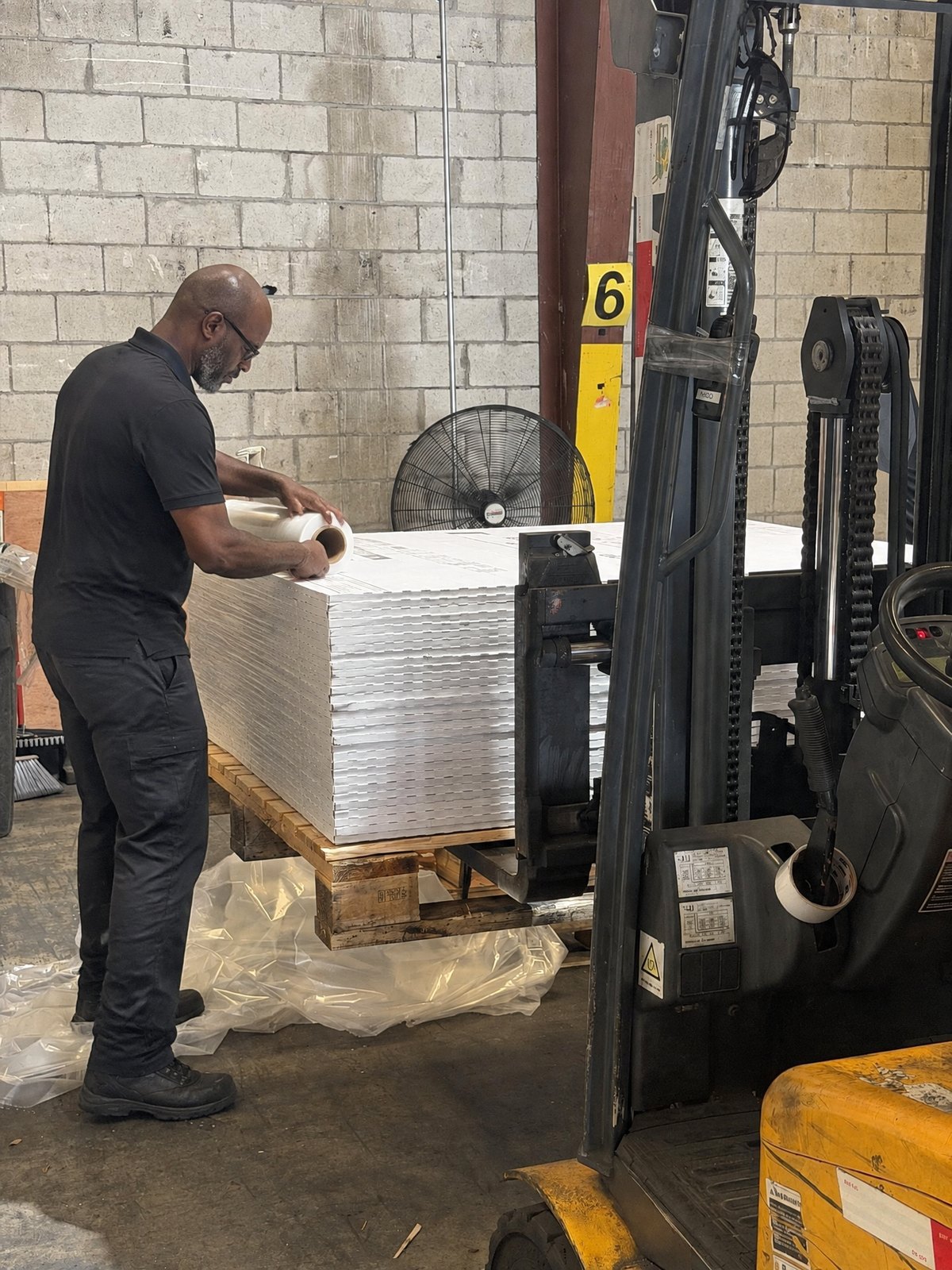 Un empleado del almacén de Porcemall envolviendo un pallet de cerámica junto a un montacargas